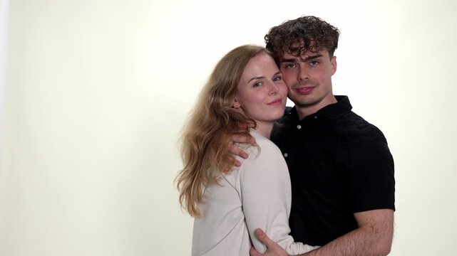 A young couple embraces with affection and love, showcasing a romantic relationship and deep connection. The man and woman are seen in a studio setting against a white background, highlighting their i
