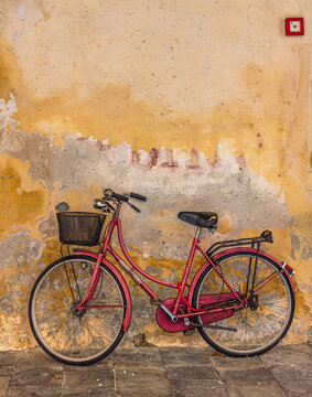 A red bicycle with a wicker basket leaning against an orange wall