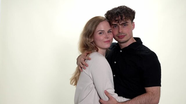 A young couple embraces affectionately against a clean white background, embodying concepts of love, romance, and strong relationships. This studio portrait captures their connection and happiness, ma
