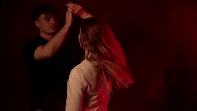 Romantic connection and fun as a young couple dances together in a moody red lit setting. This footage captures the joy and intimacy of a man and woman enjoying each other s company, commercial projec