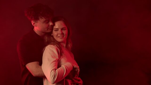 Love and intimacy concept a romantic young couple embracing in a studio setting, illuminated by vibrant purple and red neon lights. The man is seen tenderly kissing the woman s neck, conveying deep af