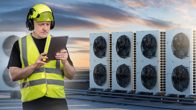 HVAC technician inspects rooftop air conditioning units using tablet during maintenance check.