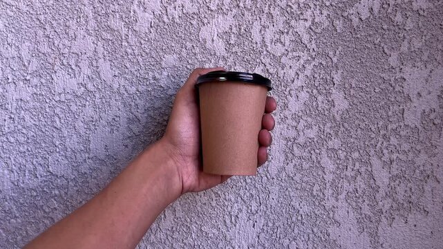 Male or men hand holding paper cup of take away drinking coffee. gray or grey wall on the background. purple, voilet, lilac. front, side.