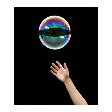Close-up of a hand reaching for a large iridescent soap bubble against a dark background with cinematic lighting.