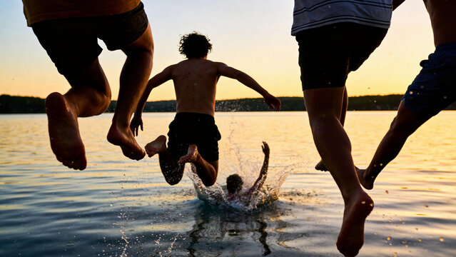 Friends jumping into lake at sunset creating splash joyful summer vacation