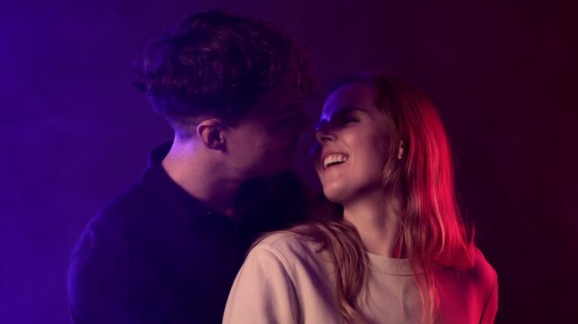 A young couple shares an intimate moment, illuminated by vibrant, colorful lighting that creates a romantic and fun atmosphere. This scene captures their close connection and expressions of joy, proje