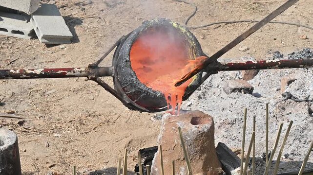 Blacksmith holding a hot crucible by the iron pliers from furnace and pouring the melting gold into the statue block. The process to making of metal statue in local Thailand traditional.