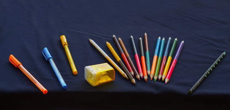 Colorful stationery set with pencils, pens, and a sharpener on a dark background