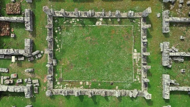 Cinematic 4K drone top-down ascending shot over the geometric stone ruins of the ancient Prytaneum in Kassope, Greece. Perfect symmetrical abstract archaeological layout.