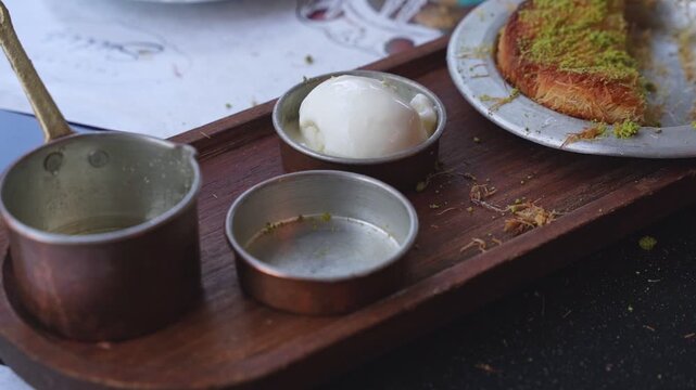 traditional Turkish kunafa dessert served with vanilla ice cream and syrup in a copper pot on a wooden tray at a restaurant.