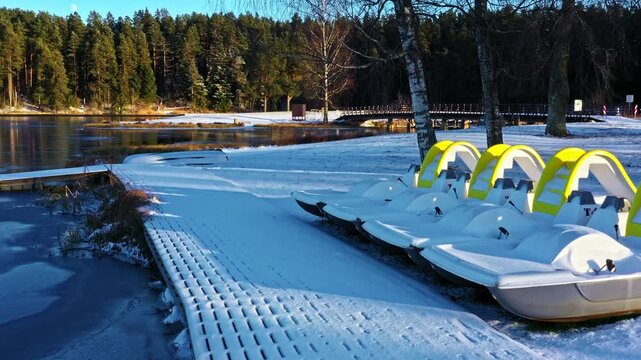 Frozen lake with dock and snow-covered pedal boats awaiting spring transition