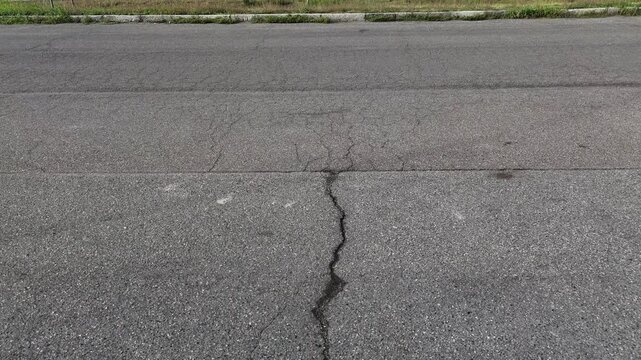 Asphalt pavement with visible longitudinal crack showing material fatigue from load stress and thermal expansion indicating road maintenance requirement
