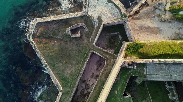 Cinematic 4K drone top-down ascending shot over the geometric stone bastions of Pantokrator Castle in Preveza, Greece. Beautiful abstract military architecture and sea foam.