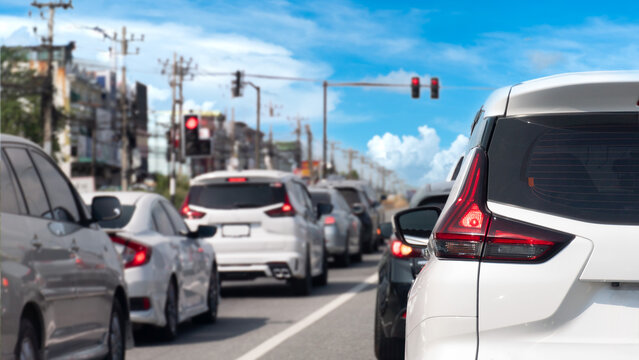 Vehicles are tightly packed in a traffic jam at a city intersection under a blue sky with light clouds. White SUV is prominent in the foreground waiting behind a long line of cars near traffic signal.