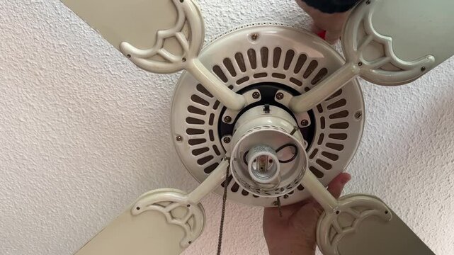 A person works on installing a light fixture on a ceiling fan, focusing on the electrical components. Useful for DIY tutorials or home improvement content.
