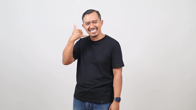 Asian Handsome man standing over white background smiling doing phone gesture with hand and fingers like talking on the telephone. Communicating concepts.