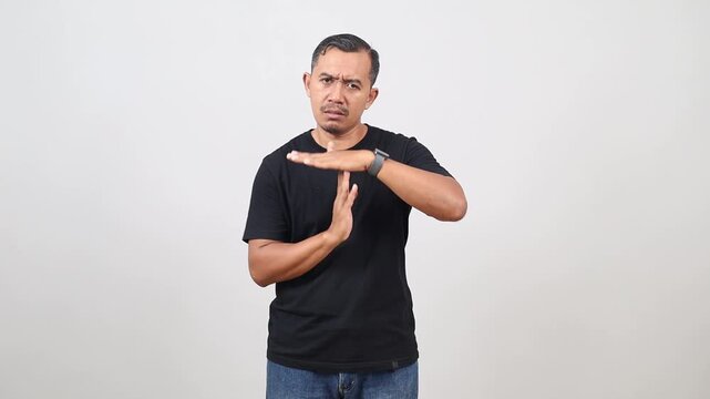 handsome Asian man standing, looking at camera and showing timeout gesture sign.