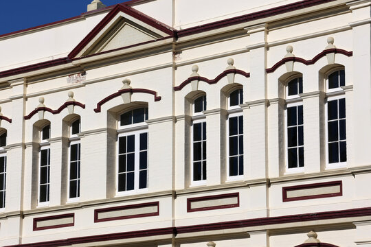 Architectural close-up of a historic building facade featuring elegant classical windows, ornate decorative trim, and traditional white plaster walls