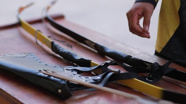 Close up video of archer hands preparing traditional bow and leather archery equipment on wooden surface wearing traditional costume