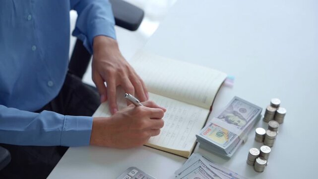 Asian businessman writing on notebook with stacking coin on table money management concept