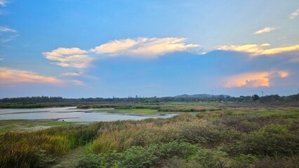 Fototapeta premium Serene Reservoir View at Sunset, Grassy Plains, Hills, and Reflections on Calm Water.