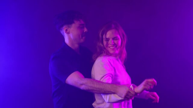 A young couple embodies love and fun, dancing and laughing together under vibrant neon lights. This footage captures their romantic relationship and party lifestyle, commercial projects, social media 