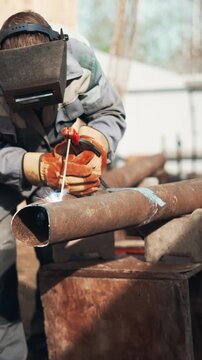 Skilled worker welds large rusty pipes outdoors using protective helmet and gloves. Bright sparks and smoke create dramatic industrial scene focused on repair work and practical craftsmanship.