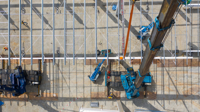 Aerial View of Construction Site: A high-angle view captures an active construction site with a crane lifting steel beams, showcasing industrial progress and building development.