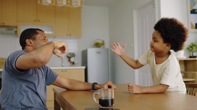 African father and son sharing playful fist bump at home kitchen.