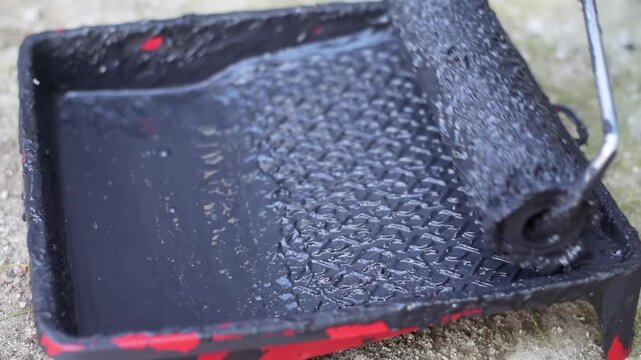 Paint roller dipping in black dye on plastic tray for home renovation projects.
