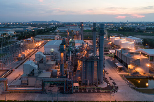 Industrial Powerhouse at Dusk: An illuminated industrial complex, likely a power generation facility, stands against the twilight sky, showcasing a network of pipes, stacks, and cooling towers.