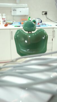 Panning across a professional dental examination room featuring a green patient chair, cuspidor, and sterile white cabinets.