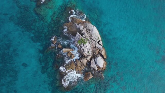 Cinematic drone pull-up shot starting top-down on a granite rock islet with trees, revealing the vast, crystal-clear turquoise waters of Anse Soleil, Mahe, Seychelles 30fps 004