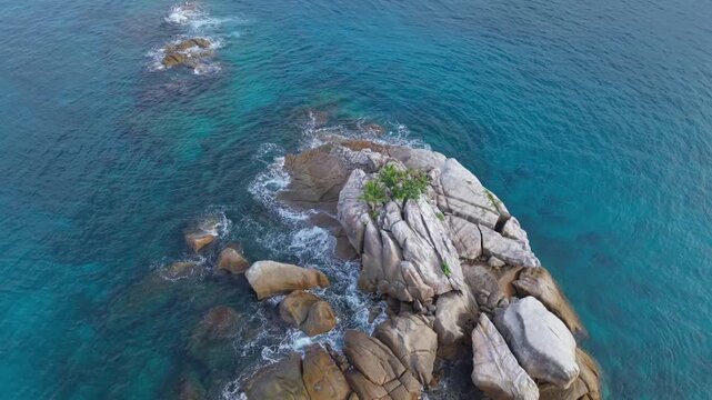 Cinematic drone reveal of a small granite rock island featuring palm trees and greenery, surrounded by crystal-clear turquoise water near Anse Soleil, Mahe, Seychelles. 30fps 007