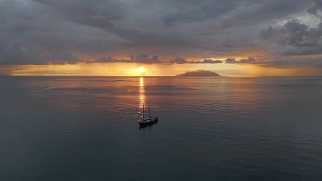 Aerial rotation around a sailing boat during a dramatic golden sunset at Beau Vallon, Mahe. Features vibrant clouds and calm Indian Ocean reflections 003