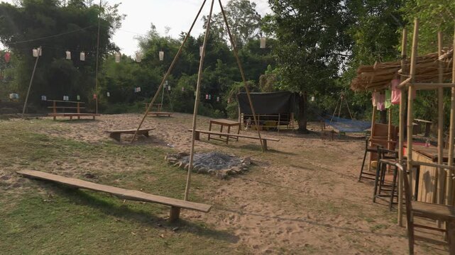 Shot of a sandy Mekong River beach area on Don Det, Laos, with a small bamboo bar, hammocks, trees and a fire pit.
