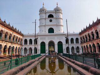 Fototapeta premium Symmetric view of the historic Hooghly Imambara courtyard featuring the iconic white clock tower, central reflection pool, and grand Islamic-Indo-European architecture in West Bengal, India.