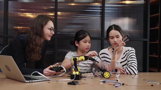 Teacher guiding students in STEM robotics classroom with coding and robotic arm experiments.