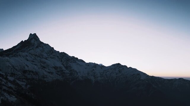 The snow-covered Fishtail peak of Machhapuchhre rises in silhouette against a soft dawn sky in the Annapurna region of Nepal.