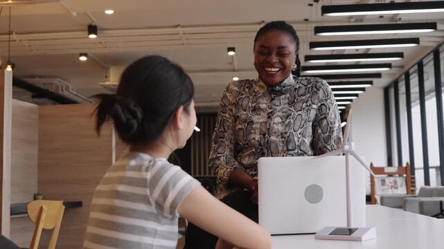 African Teacher and Asian student celebrating STEM learning achievement with high five in modern classroom.