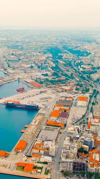 Vertical video. Thessaloniki, Greece. Aerial panorama of the historic port and city center, dense terracotta rooftops meeting the deep blue Thermaic Gulf under bright summer light. Drone footage, Dep