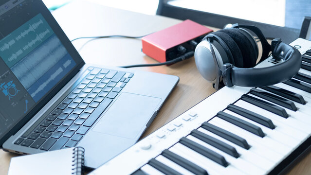 Home studio setup with laptop showing audio tracks, MIDI keyboard, headphones and audio interface for songwriting and music production.