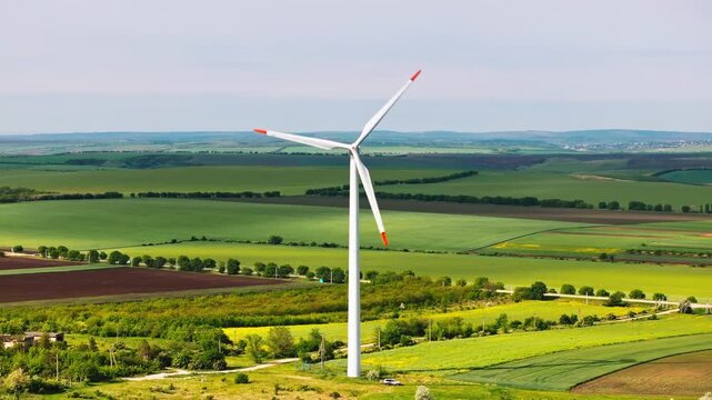 Aerial view of modern wind turbine generating clean electric power in rural farmland landscape during sunny summer day.