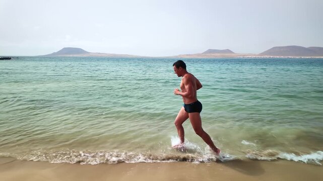 Athletic man running along the seashore on Risco beach