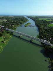 Fototapeta premium Aerial View Of Steel Bridge Spanning River With Village And Lush Green Mountain Landscape
