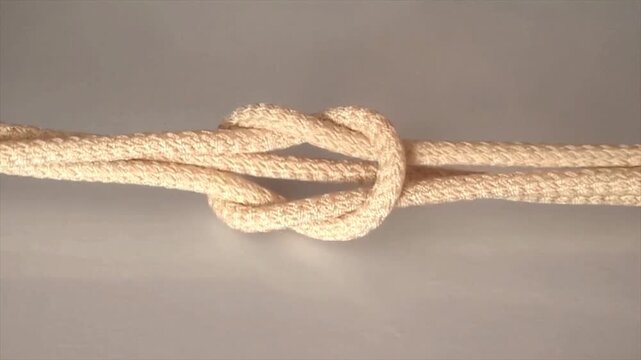 Strong rope knot close up view, white tied cord symbol of connection, strength and security concept isolated on neutral gray background, stock footage.