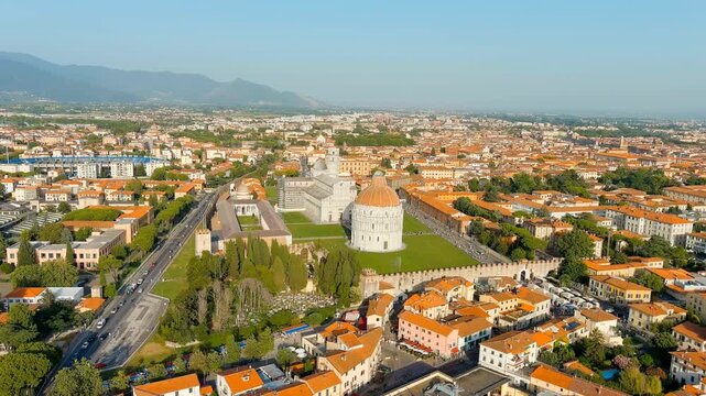 Pisa, Italy. The Baptistery of San Giovanni and Pisa Cathedral, white marble domed rotunda and Romanesque facade, Drone footage over terracotta rooftops and green lawns of Piazza dei Miracoli. Drone 
