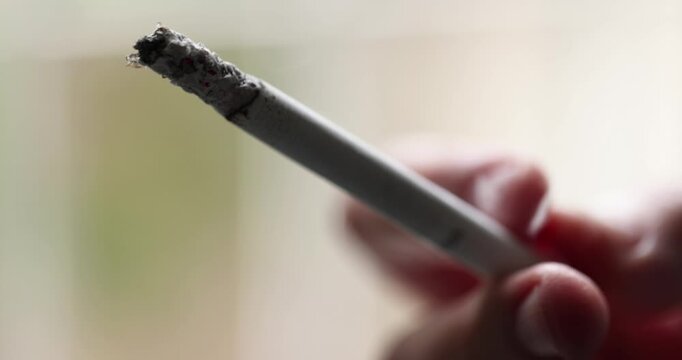 Extreme close-up view of a burning tip cigarette held between fingers on a stress day.