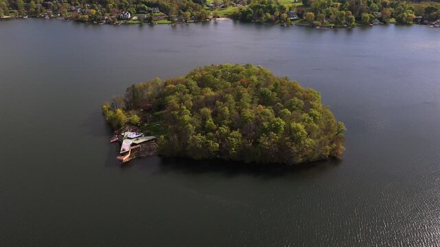Aerial view of the Massaro House on Petre Island upstate. A unique triangular house on the shoreline, with a helipad, skylight panels and trees. The camera tilted down, slowly, truck left, pan right.