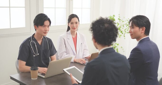 クリニックの会議室で打ち合わせをする若い医師とビジネスマン